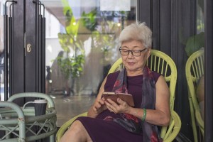 Elderly Asian woman using a mobile phone in serene backyard garden