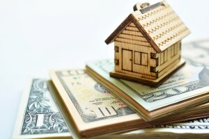 small toy wood house on stack of moeny